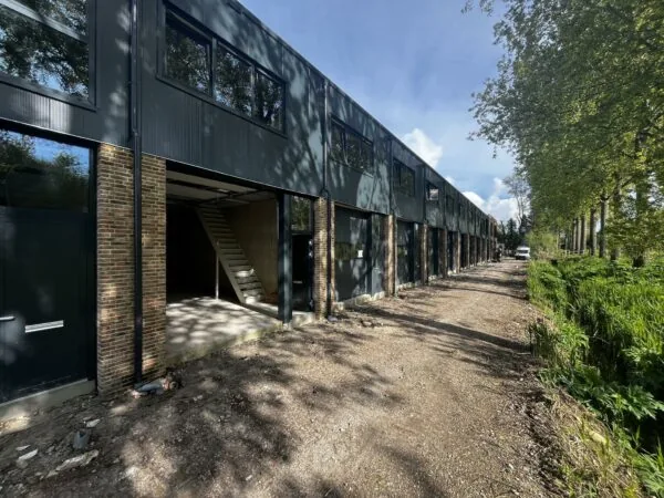 Een rij moderne bedrijfsunits aan de Broekdijk West in aanbouw, met open garages en bouwmateriaal op een onverharde weg.